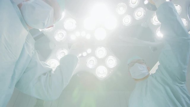 Low Angle Shot of Two Professional Surgeons Turning on Surgery Lights while Bending over Patient.  Shot on RED EPIC-W 8K Helium Cinema Camera.