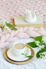 Fototapeta na wymiar Cup with white coffee, milk, pink pastel giant blanket, bedroom, morning concept, bird cherry tree flowers, book reading 