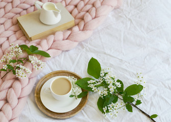 Cup with white coffee, milk, pink pastel giant blanket, bedroom, morning concept, bird cherry tree flowers, book reading 