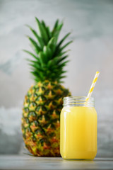 Glass jar of pineapple smoothie and whole fruit on gray background. Copy space. Summer, holiday concept. Raw, vegan, vegetarian, clean eating diet.
