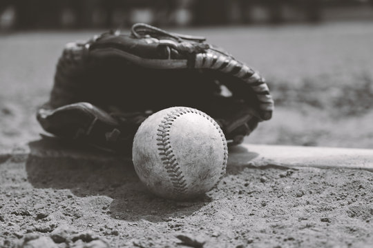 Old dirty baseball with glove on dirt field brings back nostalgia of sports memories for ball player in black and white.