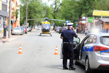 Policjant rozmawia przez telefon przy samochodzie służbowym, przed śmigłowcem w centrum miasta Opola.