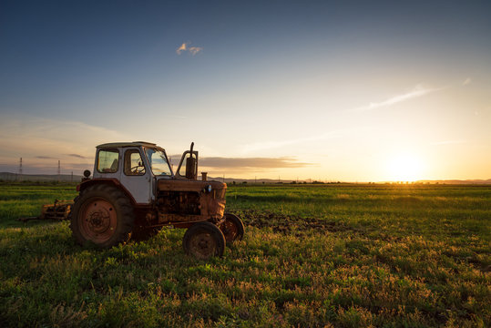 Red tractor on golden sunset sky.