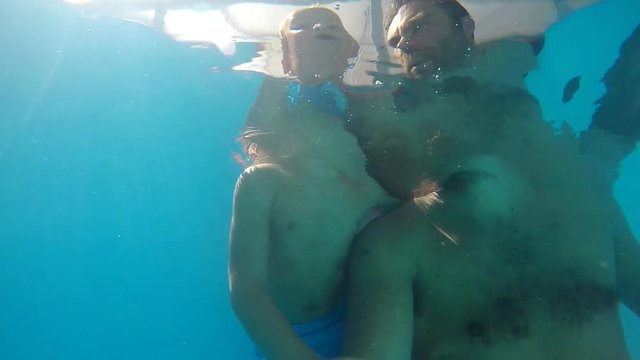 Father and son diving in the pool. View from below the water.