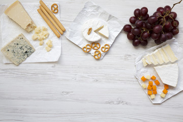 Tasting cheese with grapes, bread sticks, walnuts and pretzels on wooden background, top view. Food for romantic. Flat lay. From above. Copy space.