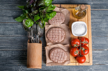 Chicken burgers cutlets on a wooden board with cherry tomatoes and spices. Top view