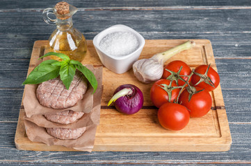 Stack of chicken burgers cutlets on a wooden board with cherry tomatoes and spices.