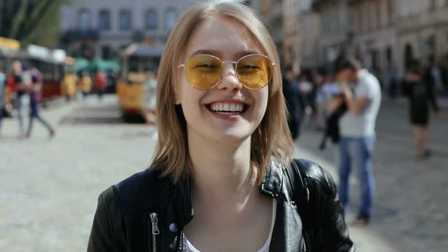 outdoors portrait of young stylish woman wearing trendy yellow sunglasses smiling brightly and looking at camera perfect smile laughing female joyful mood happiness funny girl enjoying life sunny day