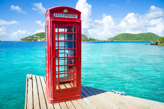 Classic red English telephone booth on a dock in the British Virgin Islands surround by beautiful turquoise Caribbean sea.