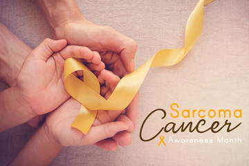 adult and child hands holding yellow gold ribbon, Sarcoma cancer Awareness month - Powered by Adobe