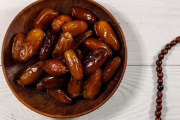 Dates fruit and rosary on white wooden table. Top view