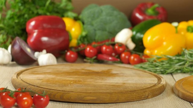 Chef takes a piece of raw juicy meat lying on a round wooden board flips throw on the board and cuts a piece of meat, in the background vegetables greens, broccoli, red pepper, red onion, garlic