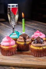 Several cupcakes on a wooden cutting board with a birthday single candle and glass of Champagne