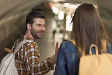 smiling male tourist with backpack giving hand to girlfriend at subway station