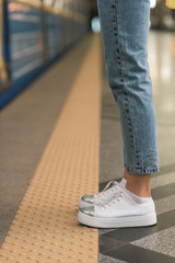 cropped image of female legs in stylish jeans and sneakers at subway station