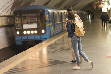 rear view of stylish couple of travelers with backpacks at metro station
