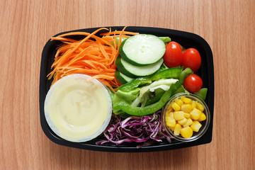 Fresh mix Salad and dressing In clear plastic box. tomato,Carrot sliced,Purple cabbage sliced, Cucumber sliced and Corn kernels on wooden floor. Ready to eat.Top view