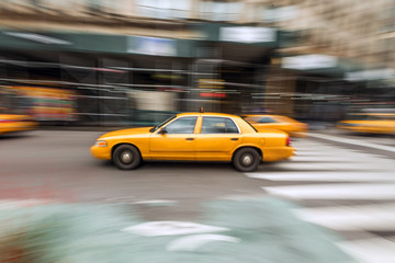 A traditional NYC taxicab drives down a Manhattan street with motion blur captured with slow shutter speed directly in image