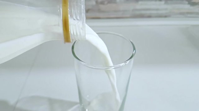fresh white milk pouring into drinking glass on kitchen background, shooting with slow motion, diet and healthy nutrition breakfast concept
