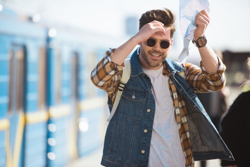 stylish male traveler in sunglasses holding map in hand at outdoor subway station