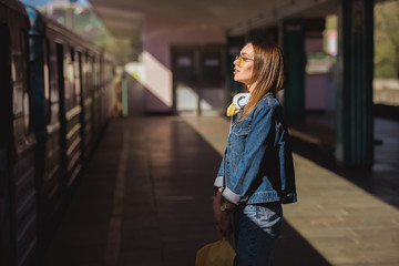 side view of stylish woman in sunglasses with headphones standing at outdoor subway station