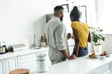 back view of african american couple looking at smartphone at kitchen