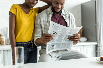 cropped image of african american couple reading newspaper at kitchen