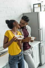 african american couple kissing while having breakfast at kitchen