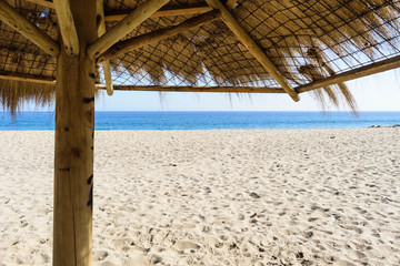 Fototapeta na wymiar Straw Beach Umbrellas on Sand Beach blue Sea Blue Sky Background. Bright Sunlight. Summer Vacation Wanderlust Traveling Concept. Copy Space