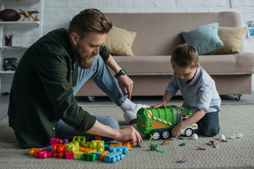 father and little son playing with toy cars together on floor at home