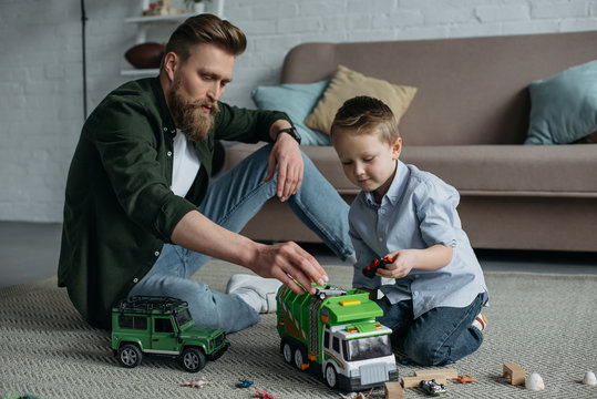 father and little son playing with toy cars together on floor at home