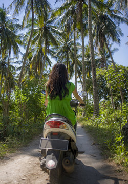 happy tourist woman riding scooter motorbike in tropical paradise jungle  with blue sky and palm trees in exploring destination and Summer holidays travel