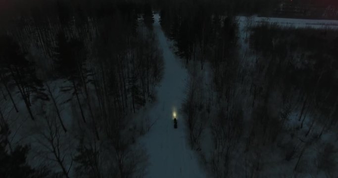 Snowmobile rides through the woods at night rear view