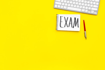 Exam concept. Lettering Exam in notebook on student's work desk on yellow backgrond top view copy space