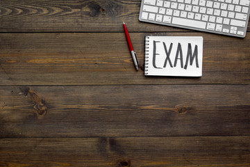 Preparing for the exam. Word Exam written in notebook on student's desk with computer on dark wooden backgrond top view space for text