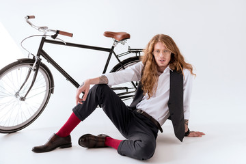 Fototapeta premium stylish tattooed businessman with curly hair sitting on floor near bicycle