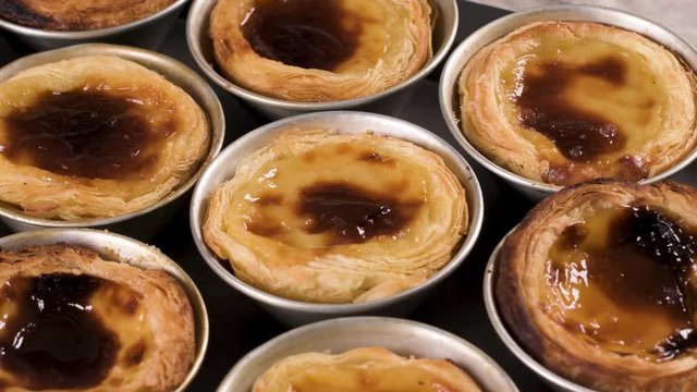 Rows of freshly cooked egg tarts, traditional portuguese dessert, pastel de nata, custard tarts on metal tray.