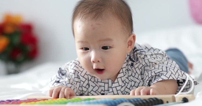 Cute asian happy 7 month baby boy in diaper lying and playing. Portrait of a crawling baby on the bed.