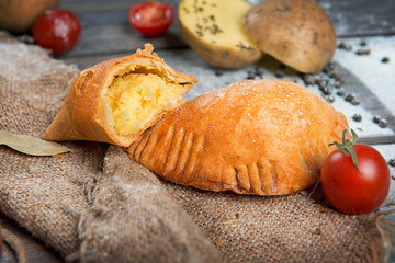 Pies with potatoes on a dark wooden table top view. Advertising still life from baking.