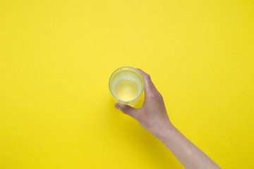 Female hand holding a glass of clean water on a yellow background. Flat lay, top view