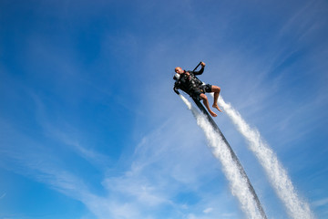 Fototapeta premium Thrillseeker, man, athlete strapped to Jet Lev, levitation soars into a blue sky with wispy clouds