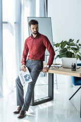 handsome young businessman with newspaper leaning back on workplace
