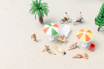 Miniature people wearing swimsuit relaxing on the beach