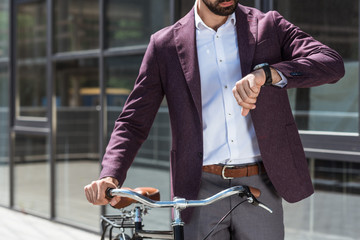 cropped shot of man in stylish suit with vintage bicycle looking at watch