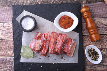 Raw fresh meat, uncooked lamb or beef ribs with pepper, garlic, salt, bay leaves and spices on dark stone background, Ready for cooking. copy space.