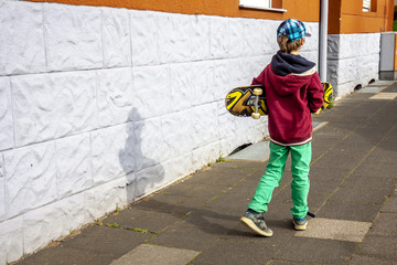 Young walking along white wall with longboard