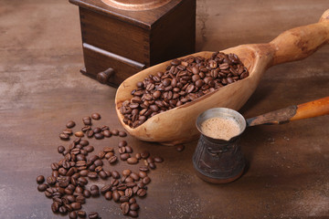 Old wooden scoop with coffee beans, coffee grinder and Cezve on dark stone table.