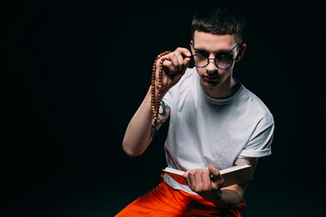 Male prisoner holding rosary and reading bible on dark background