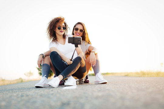 Young women siting together on longboard in road taking selfie