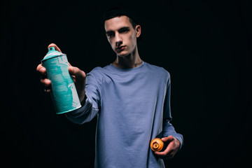 Young man painting with spray paint isolated on black
